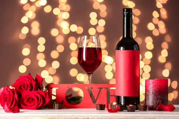 Glass of wine, word LOVE, rose flowers and bottle on table against blurred lights. Valentine\'s Day celebration