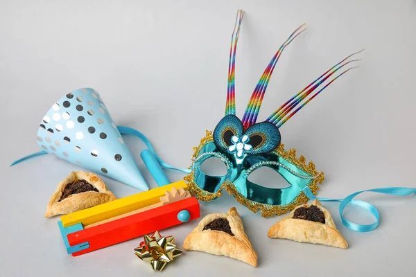 Hamantaschen cookies, carnival mask, party hat and rattle for Purim holiday on grey background