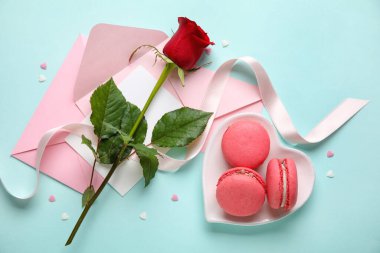 Tasty macaroons, rose flower and envelopes on blue background. Valentine's Day celebration