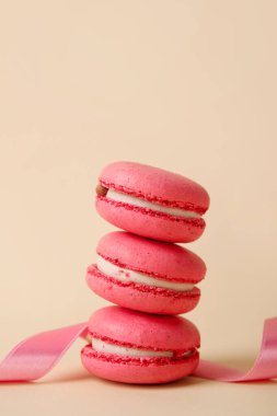 Tasty macaroons and pink ribbon on beige background. Valentine's Day celebration