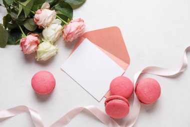 Tasty macaroons, rose flowers and blank greeting card on white background. Valentine's Day celebration