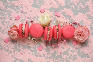 Composition with tasty macaroons, roses and gypsophila flowers on pink grunge background. Valentine's Day celebration