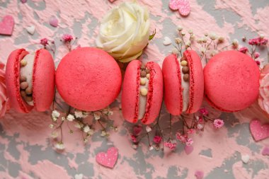 Composition with tasty macaroons, roses and gypsophila flowers on pink grunge background. Valentine's Day celebration
