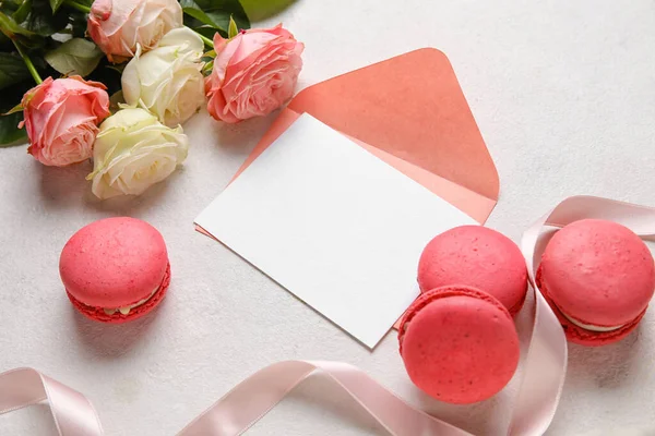 Tasty macaroons, rose flowers and blank greeting card on white background. Valentine's Day celebration