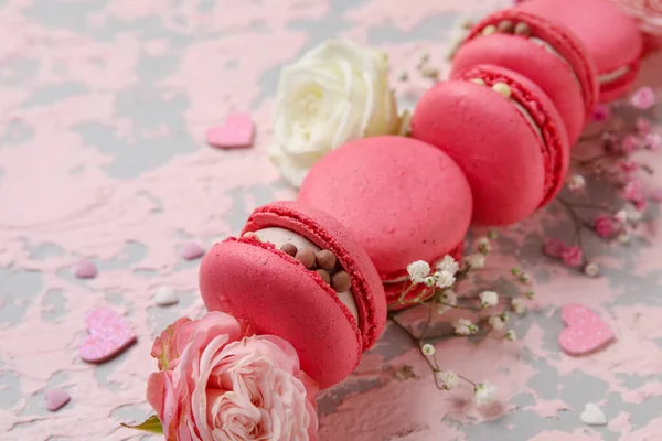 Composition with tasty macaroons, roses and gypsophila flowers on pink grunge background. Valentine's Day celebration