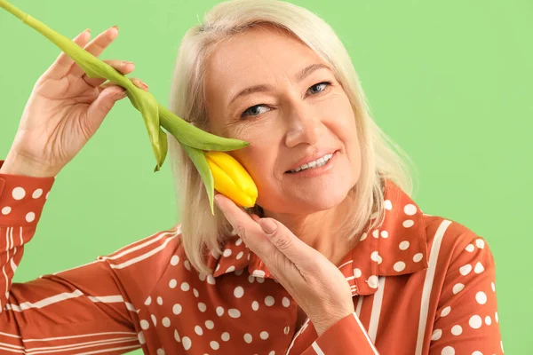 Beautiful mature woman with tulip on green background