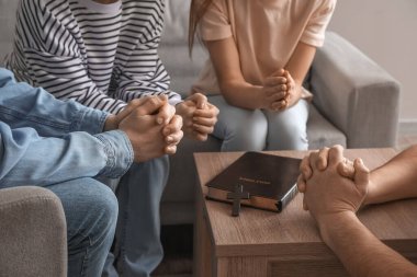 Group of people praying with Holy Bible at home, closeup