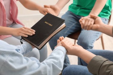 Group of people praying with Holy Bible in room, closeup
