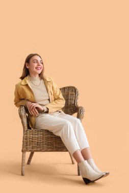 Young woman sitting in wicker armchair on beige background