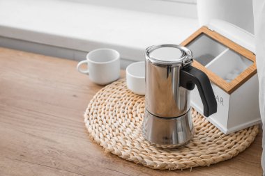 Wicker coaster with geyser coffee maker and cups on kitchen counter