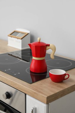 Geyser coffee maker on electric stove and cup on counter in kitchen near grey wall