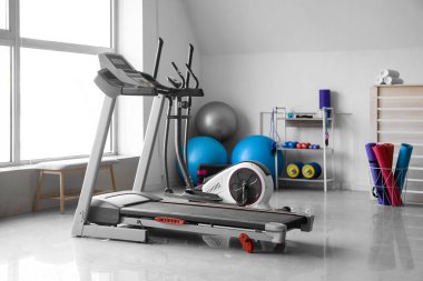Interior of gym with modern treadmill and sport equipment near window