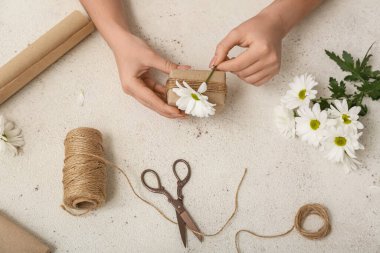 Female hands with gift box, rope, scissors and flowers on light background. Women's Day celebration
