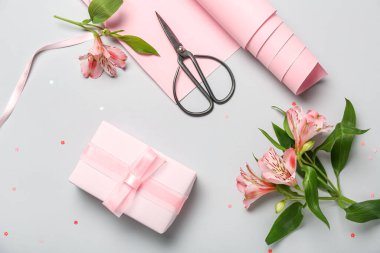 Composition with gift box, wrapping paper, scissors and alstroemeria flowers on light background. Women's Day celebration