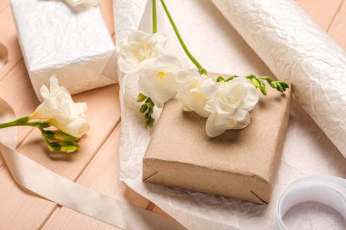 Composition with gift boxes, wrapping paper and beautiful freesia flowers on color wooden background, closeup. Women's Day celebration