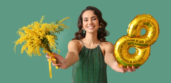 Smiling young woman with mimosa flowers and balloon in shape of figure 8 on green background. International Women\'s Day