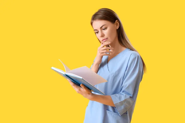 Female medical intern reading book on yellow background