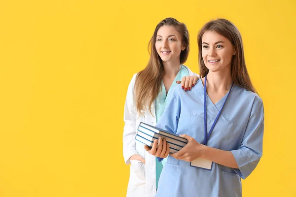 Female doctor and intern with books on yellow background