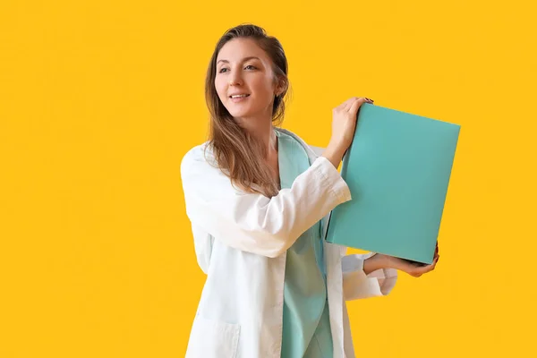 Female doctor with folder on yellow background