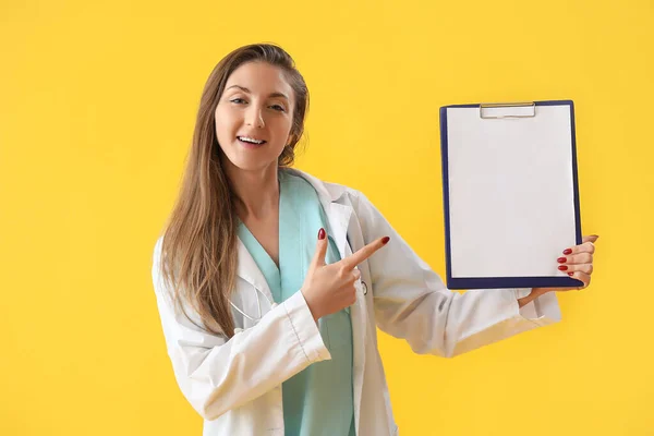 Female doctor pointing at clipboard on yellow background