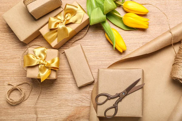 Composition with gift boxes, wrapping paper, rope, scissors and tulip flowers on wooden background. Women\'s Day celebration