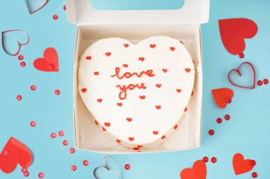Opened box with heart-shaped bento cake and hearts on blue background. Valentine's Day celebration