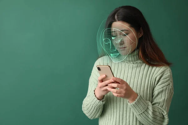 Young Asian woman with mobile phone using facial recognition system on green background