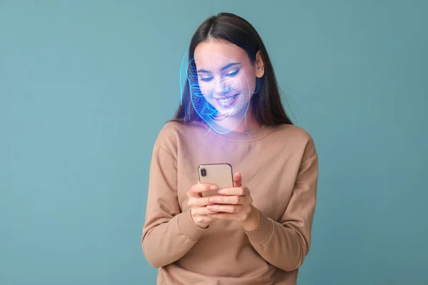 Young woman with mobile phone using facial recognition system on blue background