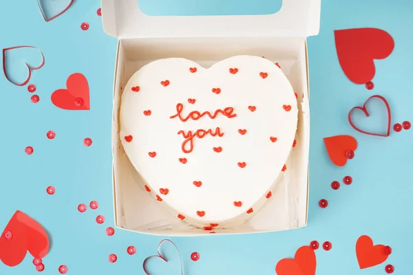 Opened box with heart-shaped bento cake and hearts on blue background. Valentine\'s Day celebration
