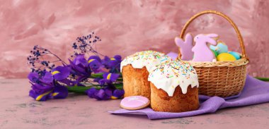 Easter cakes with iris flowers and wicker basket with eggs and cookies on pink background