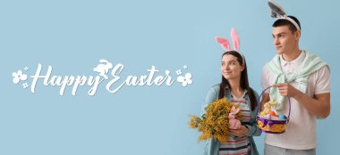 Banner with happy young couple holding Easter eggs, bunnies and mimosa flowers on grey background