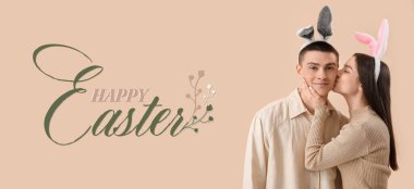 Easter banner with young woman in bunny ears kissing her boyfriend on beige background