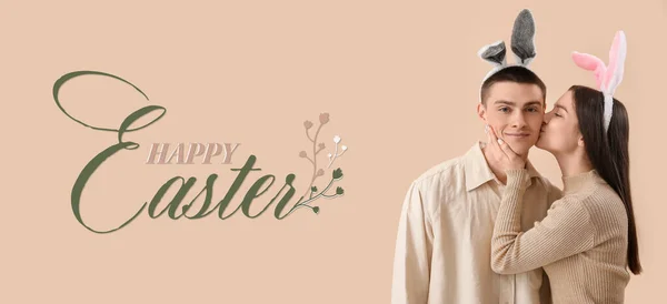 Easter banner with young woman in bunny ears kissing her boyfriend on beige background