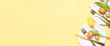 Table setting with Easter eggs and flowers on yellow background with space for text