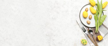 Table setting with Easter eggs and flowers on light background with space for text