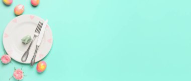 Table setting with Easter eggs and flowers on mint background with space for text
