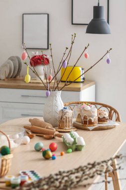Vase with tree branches, Easter cakes and eggs on dining table in kitchen