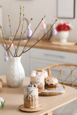 Vase with tree branches and tasty Easter cakes on dining table in kitchen