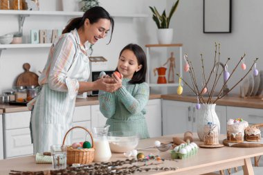 Little girl with Easter eggs and her mother cooking in kitchen