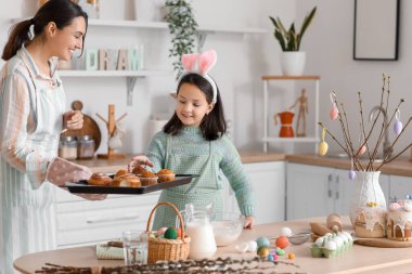 Little girl and her mother with cupcakes in kitchen on Easter day