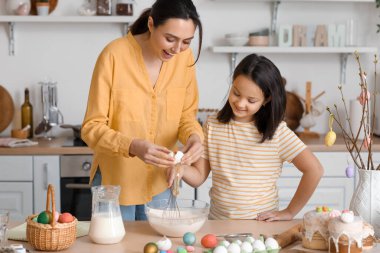 Little girl and her mother making dough for Easter cake in kitchen