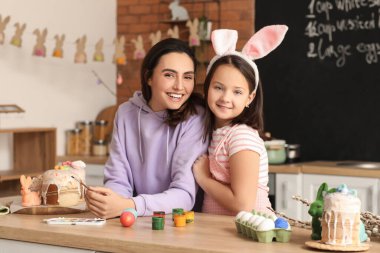 Little girl and her mother painting Easter eggs at table in kitchen