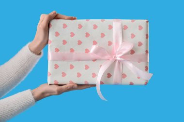 Female hands holding gift on blue background. Valentine's Day celebration