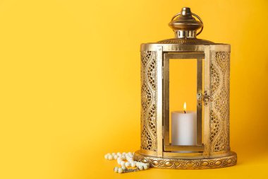 Lantern with candle and prayer beads on yellow background. Islamic New Year celebration