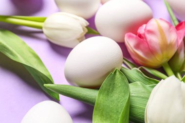 Easter eggs and tulip flowers on lilac background, closeup