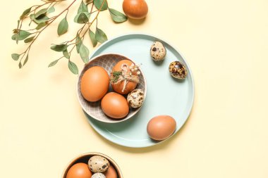 Plate and bowl with Easter eggs on yellow background