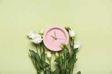 Alarm clock and beautiful eustoma flowers on green background
