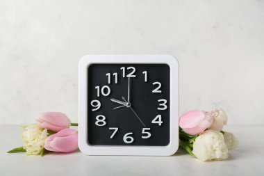 Alarm clock and beautiful tulip flowers on light background