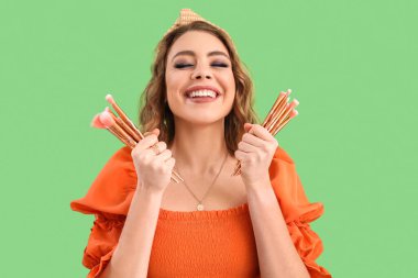 Beautiful happy young woman with makeup brushes on green background