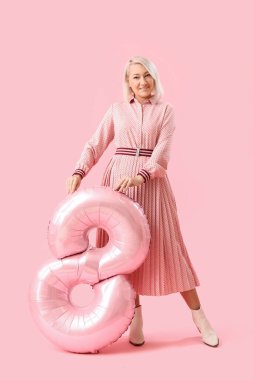 Beautiful mature woman with balloon in shape of figure 8 on pink background. International Women's Day